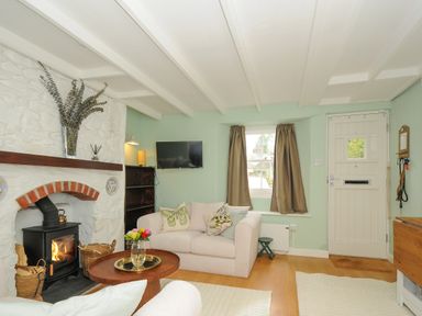 A living room with a wood stove in a stone fireplace a sofa coffee table tv and front door at 15 The Moors in Lostwithiel