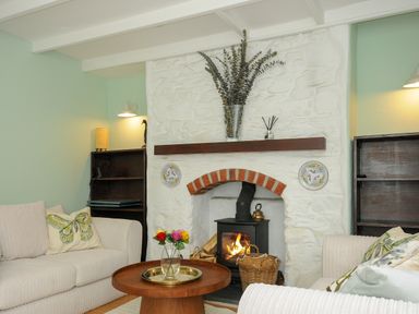 A living room with a fireplace two sofas a round wooden table and wooden bookshelves at 15 The Moors in Lostwithiel