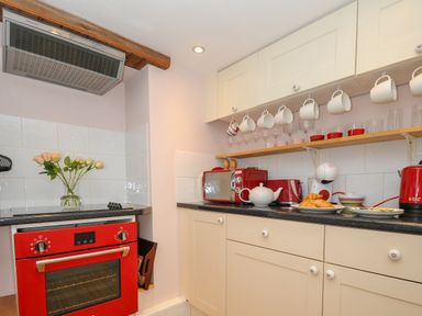 A kitchen with a red oven a microwave a teapot and cups hanging on a rack at 15 The Moors in Lostwithiel