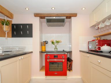 A kitchen with a red oven and microwave beige cabinets and a black countertop at 15 The Moors in Lostwithiel