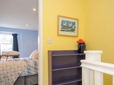 A hallway with a dark purple shelf and framed picture above with a blue bedroom visible through the doorway at 15 The Moors in Lostwithiel