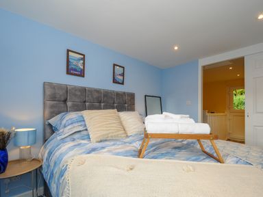 A bedroom with a gray upholstered headboard blue bedding and a tray with towels on the bed at 15 The Moors in Lostwithiel