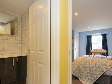 A bathroom with tiled walls and a mirror next to a bedroom with a bed and rolled towels on a tray at 15 The Moors in Lostwithiel