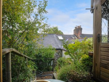 A garden area with plants and trees viewed from a wooden door with a table and railing near houses with slate roofs at 15 The Moors in Lostwithiel