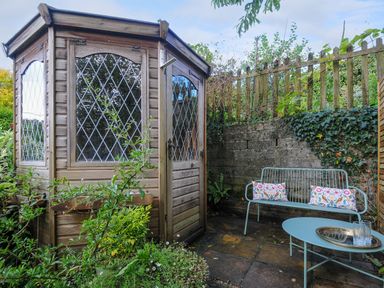 A small garden area with a wooden summerhouse a metal bench with cushions and a table at 15 The Moors in Lostwithiel