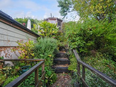 A garden path with wooden steps and railings surrounded by plants leading to a wooden gazebo at 15 The Moors in Lostwithiel