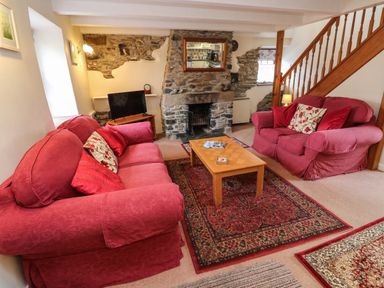 A living room with two red sofas a wooden coffee table and a stone fireplace at Swallow Cottage in Mawgan