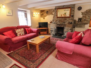 A living room with two red sofas a wooden coffee table and a stone fireplace at Swallow Cottage in Mawgan