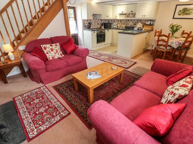 A living room with red sofas a wooden coffee table and kitchen and dining area in the background at Swallow Cottage in Mawgan