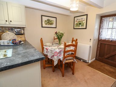 A dining area with a round table set for four and wooden chairs next to a countertop and wooden door at Swallow Cottage in Mawgan
