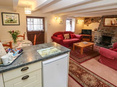 A living room with red sofas a wooden coffee table a stone fireplace and a dining table near a wooden door at Swallow Cottage in Mawgan