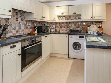 A kitchen with an oven washing machine microwave and sink at Swallow Cottage in Mawgan