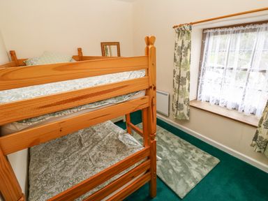 A bedroom with a wooden bunk bed a window with curtains and a rug on the floor at Swallow Cottage in Mawgan