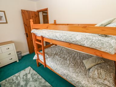 A bedroom with wooden bunk beds patterned bedding a white chest of drawers and a green carpet at Swallow Cottage in Mawgan