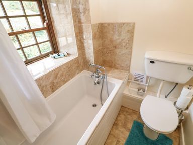 A bathroom with a bathtub next to a window and a toilet with toilet paper at Swallow Cottage in Mawgan