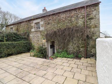 A stone cottage exterior with a tiled patio and climbing plants at Swallow Cottage in Mawgan
