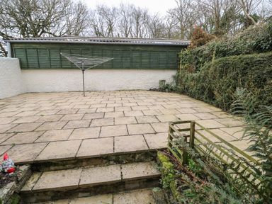 An outdoor paved patio with stairs leading up to it a rotary clothesline and garden gnome at Swallow Cottage Mawgan