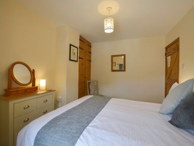A bedroom with a bed and pillows a dresser with a mirror a chair wooden wardrobe and door at Swallow Cottage in Mawgan