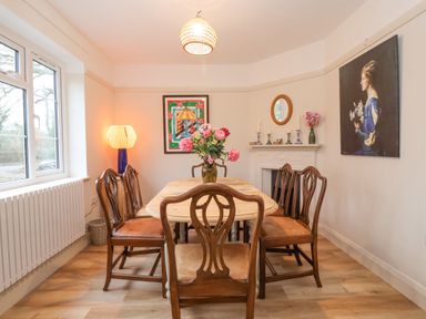 A dining room with wooden table and chairs a vase with flowers on the table paintings on the walls and a lamp by the window at 3 Chantry Cottages in Campsea Ashe near Woodbridge