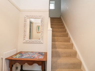 A carpeted staircase next to a wooden table with a colorful map and a framed mirror on the wall at 3 Chantry Cottages Campsea Ashe near Woodbridge