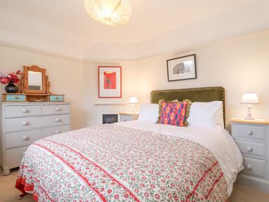 A bedroom with a bed covered with a floral patterned quilt two bedside tables with lamps a dresser with a mirror and flowers on top at 3 Chantry Cottages Campsea Ashe near Woodbridge