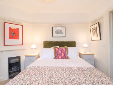 A bedroom with a double bed, two bedside tables with lamps, framed pictures on walls and a small fireplace at 3 Chantry Cottages Campsea Ashe near Woodbridge