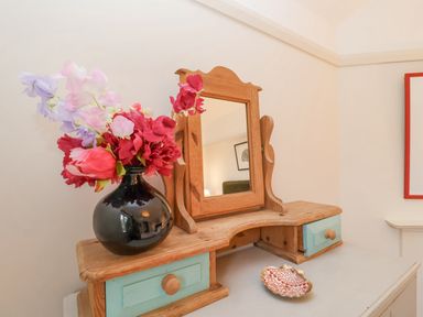 A wooden dressing table with a mirror a black vase with flowers and a decorative dish at 3 Chantry Cottages in Campsea Ashe near Woodbridge