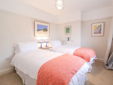 A bedroom with two twin beds with white bedding and orange patterned throws two blue table lamps on a small wooden table and framed artwork on the walls at 3 Chantry Cottages Campsea Ashe near Woodbridge