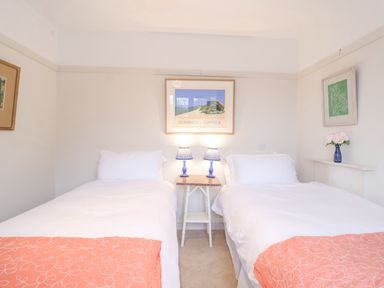 A bedroom with two single beds with white bedding and orange throws with a nightstand between and framed artworks on the walls at 3 Chantry Cottages Campsea Ashe near Woodbridge