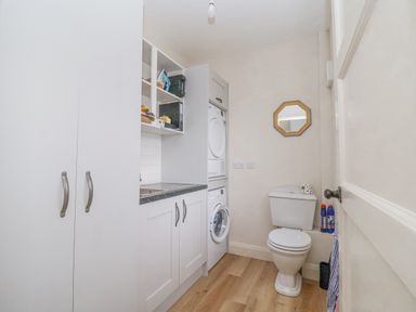 A utility room with a washing machine and dryer stacked next to a toilet with a small mirror above at 3 Chantry Cottages Campsea Ashe near Woodbridge