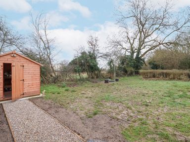 A garden with a wooden shed a gravel path a clothesline and trees at 3 Chantry Cottages Campsea Ashe near Woodbridge