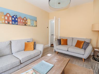 A living room with two gray sofas and orange and gray cushions at The Corner Cottage in Aldeburgh