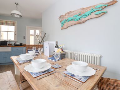 A dining table set with white bowls and wine glasses in a kitchen at The Corner Cottage in Aldeburgh