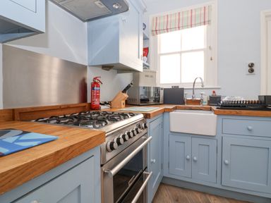 A kitchen with a gas stove wooden countertops a sink and a window at The Corner Cottage in Aldeburgh
