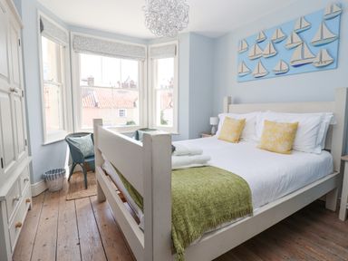 A bedroom with a large bed two yellow pillows green throw blanket two chairs by a bay window and boat decorations on the wall at The Corner Cottage in Aldeburgh