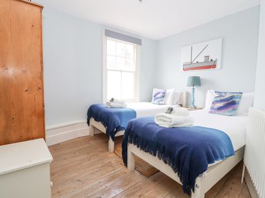 A bedroom with two single beds blue blankets wooden floor and a wooden wardrobe at The Corner Cottage in Aldeburgh