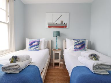 A bedroom with two single beds with blue blankets and abstract pillows at The Corner Cottage in Aldeburgh
