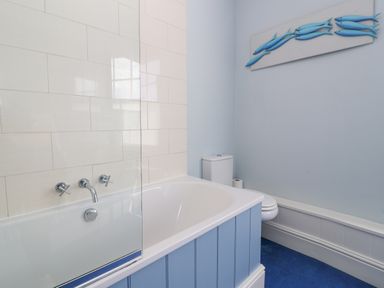 A bathroom with a bathtub a toilet and blue fish wall art at The Corner Cottage in Aldeburgh