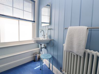 A bathroom with a sink mirror towel on radiator and blue stool at The Corner Cottage in Aldeburgh