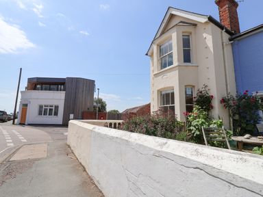A street view with houses and a garden with flowers and a wooden chair at The Corner Cottage in Aldeburgh