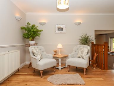 Two armchairs with cushions around a small wooden table with a lamp in a room with wooden floor and plants at Hole Park in Holsworthy