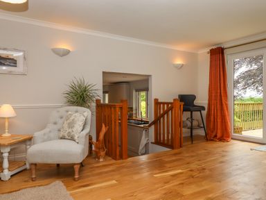 A living room with a white armchair a wooden side table and orange curtains at Hole Park in Holsworthy