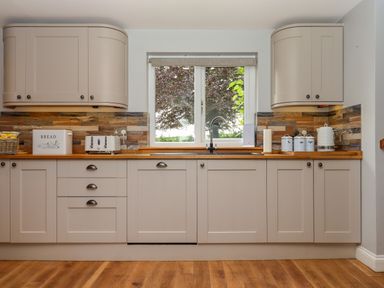 A kitchen with beige cabinets wooden countertop a window above the sink and kitchen appliances at Hole Park in Holsworthy