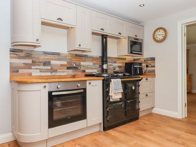 A kitchen with white cabinets wooden countertops a black stove an oven a microwave and a wall clock at Hole Park in Holsworthy
