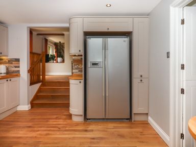 A kitchen with wooden flooring a silver double door refrigerator stairs leading to another room with plants near a window at Hole Park in Holsworthy