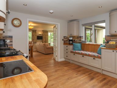 A kitchen with a wooden countertop and built in cabinets with a seating area by the window at Hole Park in Holsworthy