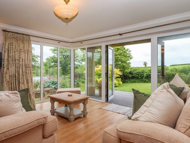 A living room with sofas and pillows and a wooden coffee table next to glass doors opening to a garden at Hole Park in Holsworthy