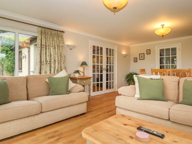 A living room with beige sofas and green cushions a wooden coffee table and a dining area in the background at Hole Park in Holsworthy