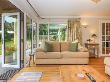 A living room with a beige sofa and green pillows near glass doors leading to a garden at Hole Park in Holsworthy