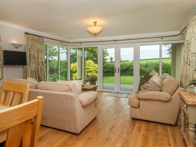 A sitting room with beige sofas wooden floor and large windows with garden view at Hole Park in Holsworthy